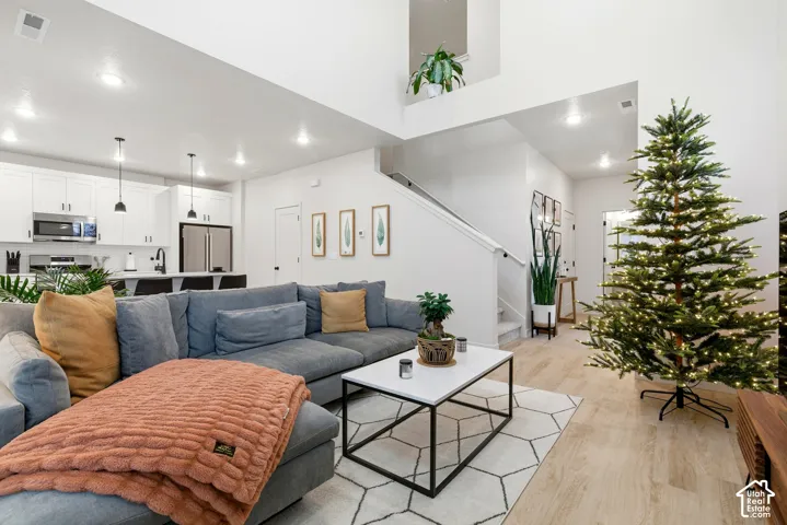 Open-concept living area featuring high ceilings, wood-finish flooring, a contemporary kitchen with white cabinetry, stainless steel appliances, and a breakfast bar