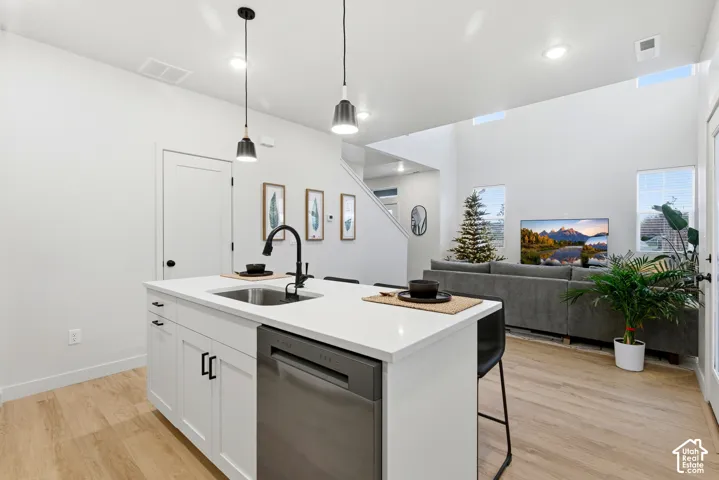 Kitchen island featuring white cabinetry, a stainless steel dishwasher, a single-basin sink with a matte black faucet, and pendant lighting