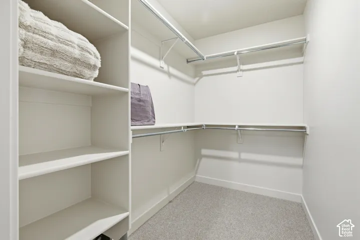 Walk-in closet featuring built-in shelving, multiple hanging rods, and light-toned carpet flooring
