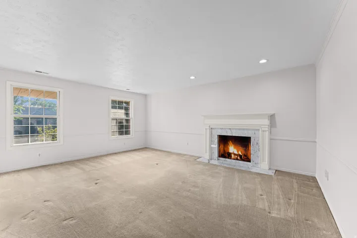 White marble fireplace with a classic mantel, recessed lighting, two double-hung windows, and light-toned carpeting