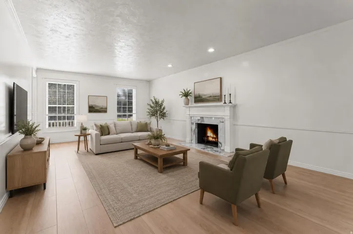 Bright and spacious living room featuring a wood-finish plank floor, recessed ceiling lighting, and a gas fireplace with white mantel and surround