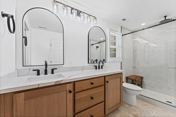 Spa-inspired primary bathroom featuring a dual-sink vanity with warm wood cabinetry, white quartz countertops, and matte black hardware