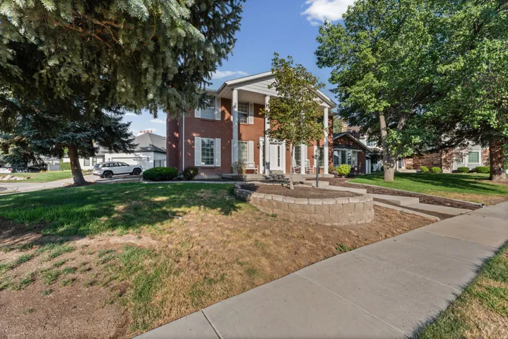 Brick exterior with white columns and shuttered windows, featuring a terraced front yard with a stone-block retaining wall
