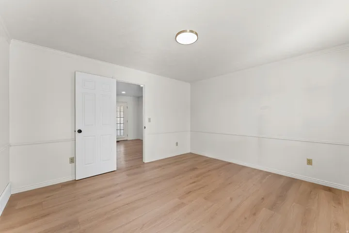 Spacious room featuring wood-finish flooring, white walls, wainscoting, and crown molding