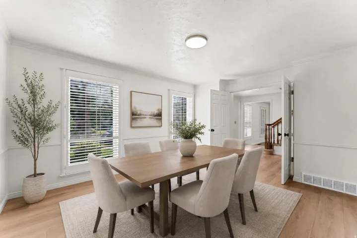Dining area featuring wood-finish flooring, white walls with wainscoting, and crown molding
