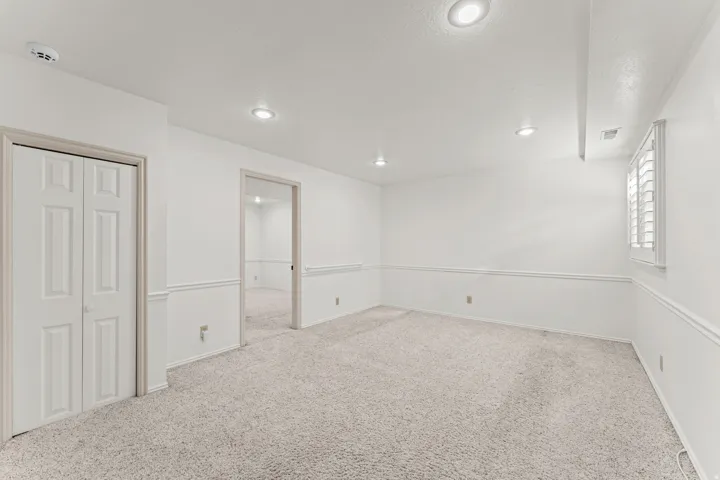 Spacious finished basement featuring neutral carpet flooring, recessed ceiling lighting, and crisp white walls with chair rail molding