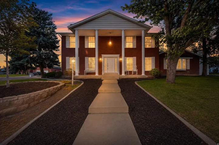 Classic brick Colonial featuring a symmetrical facade with white columns and a welcoming covered portico