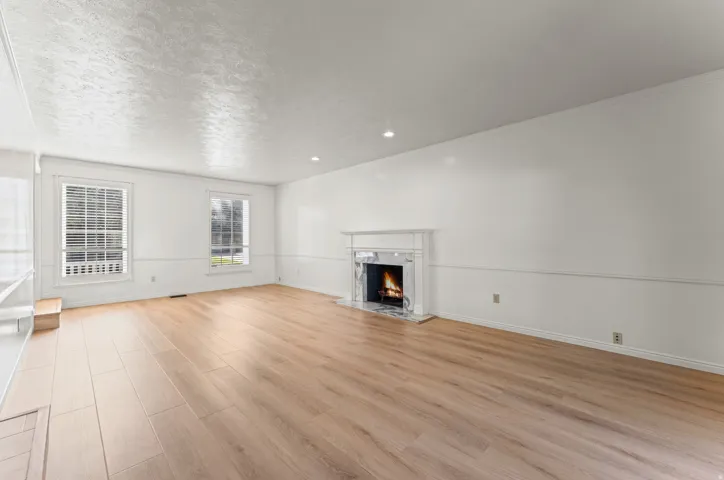 Spacious living room flooded with natural light through multiple windows, featuring newly refinished wood-finish flooring throughout