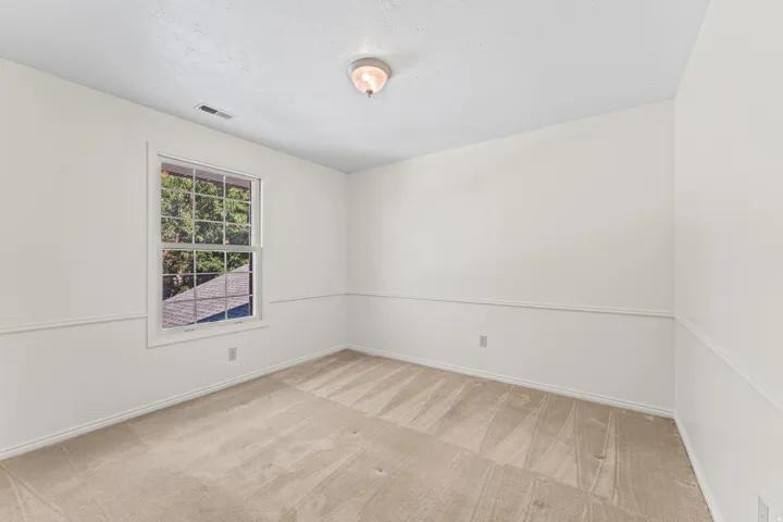 Bright secondary bedroom featuring neutral wall finishes, wood-finish flooring with linear plank detailing, and a large double-hung window with exterior views