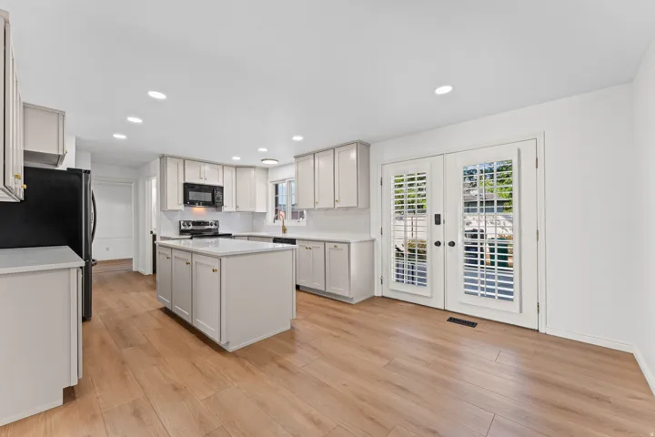 Bright kitchen featuring light wood-finish flooring, white cabinetry with gold-tone hardware, and a center island with a white countertop