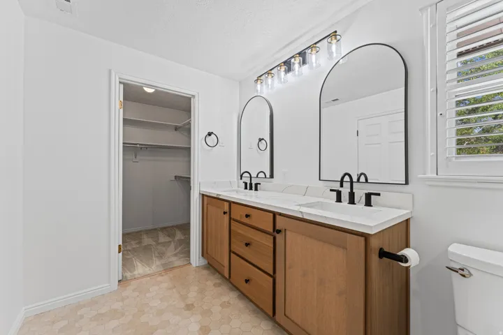 Dual vanity with wood-finish cabinetry, white countertops, and matte black fixtures