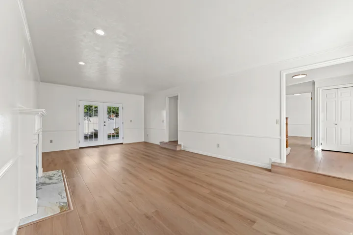 Spacious primary living area showcasing gleaming wood-finish flooring throughout, crisp white walls, and abundant natural light from dual French doors