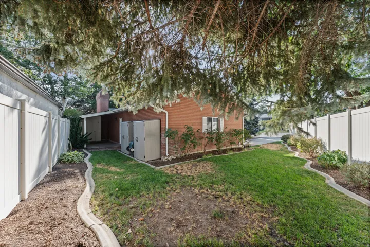 Brick exterior home featuring a spacious backyard with mature tree canopy, manicured lawn, curved hardscape edging, and detached garage structure