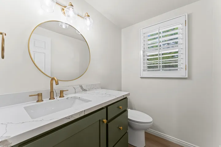 Elegant bathroom vanity featuring a dark green cabinetry base with brass hardware, white marble countertop, and an integrated rectangular sink