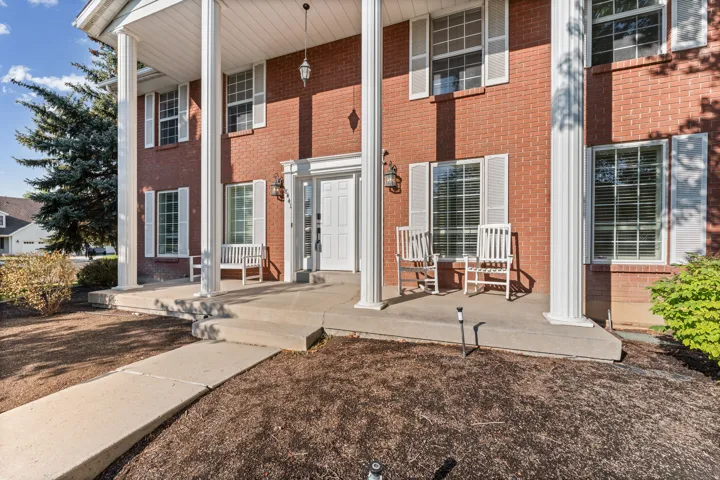 Brick exterior featuring a covered portico with white columns, a white front door, and white window shutters
