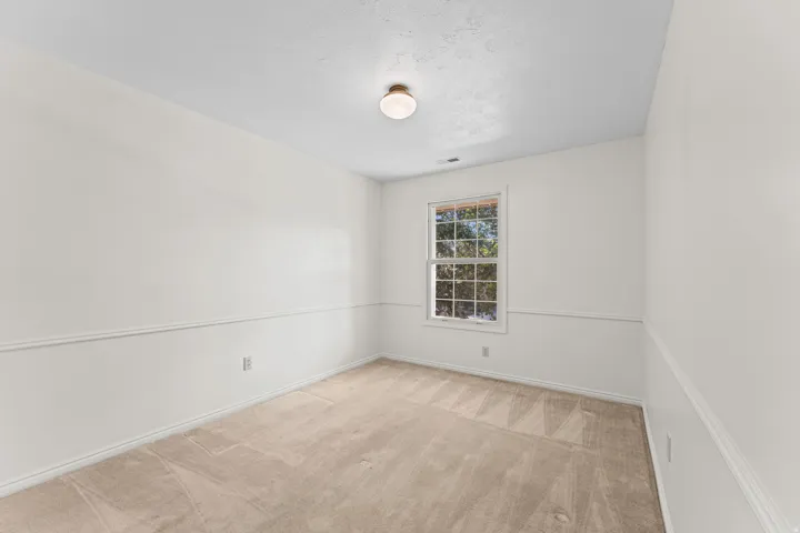 Bright bedroom featuring hardwood-finish flooring, a large double-hung window with gridded panes, and neutral white walls accented with wainscoting