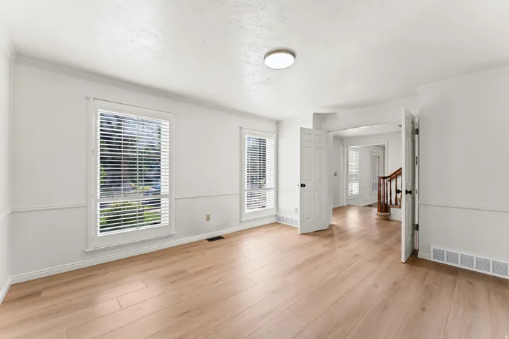 Spacious interior room featuring light wood-finish flooring, white walls with wainscoting, and two large windows with blinds