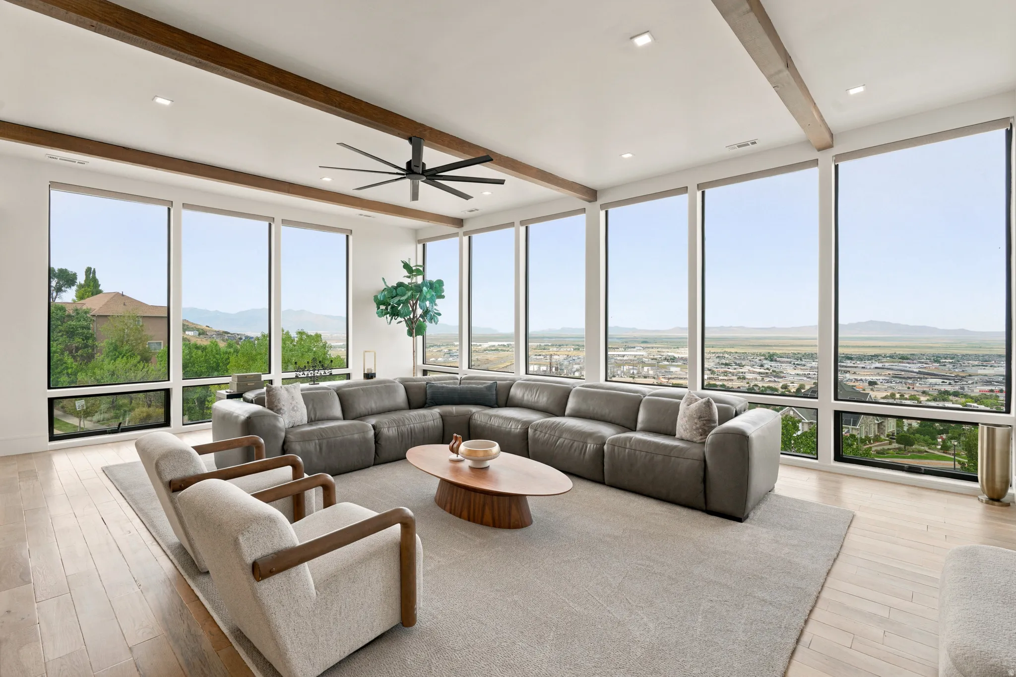 Spacious living area featuring expansive floor-to-ceiling windows, wood-finish flooring, exposed ceiling beams, recessed lighting, and a modern ceiling fan