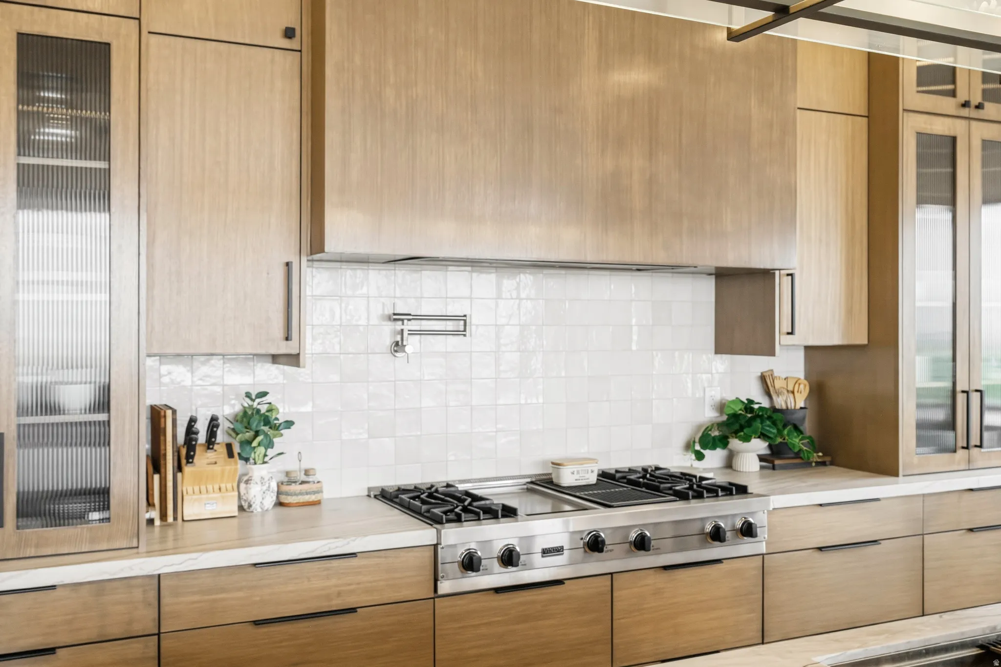 Gourmet kitchen featuring a stainless steel range, white subway tile backsplash, pot filler, wood-finish cabinetry, and glass-front upper cabinets