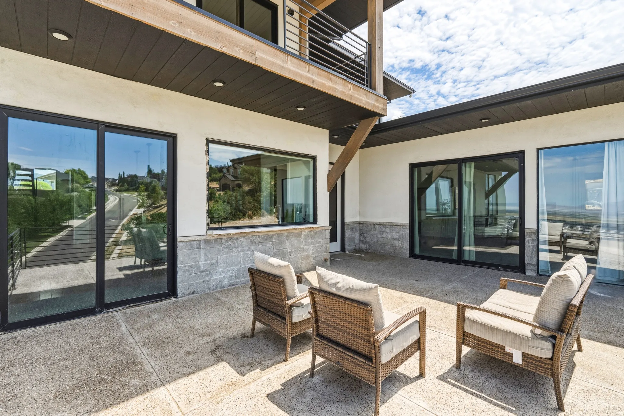Stucco exterior with stone veneer accents, multiple large sliding glass doors, a concrete patio, and a second-story balcony with metal railings