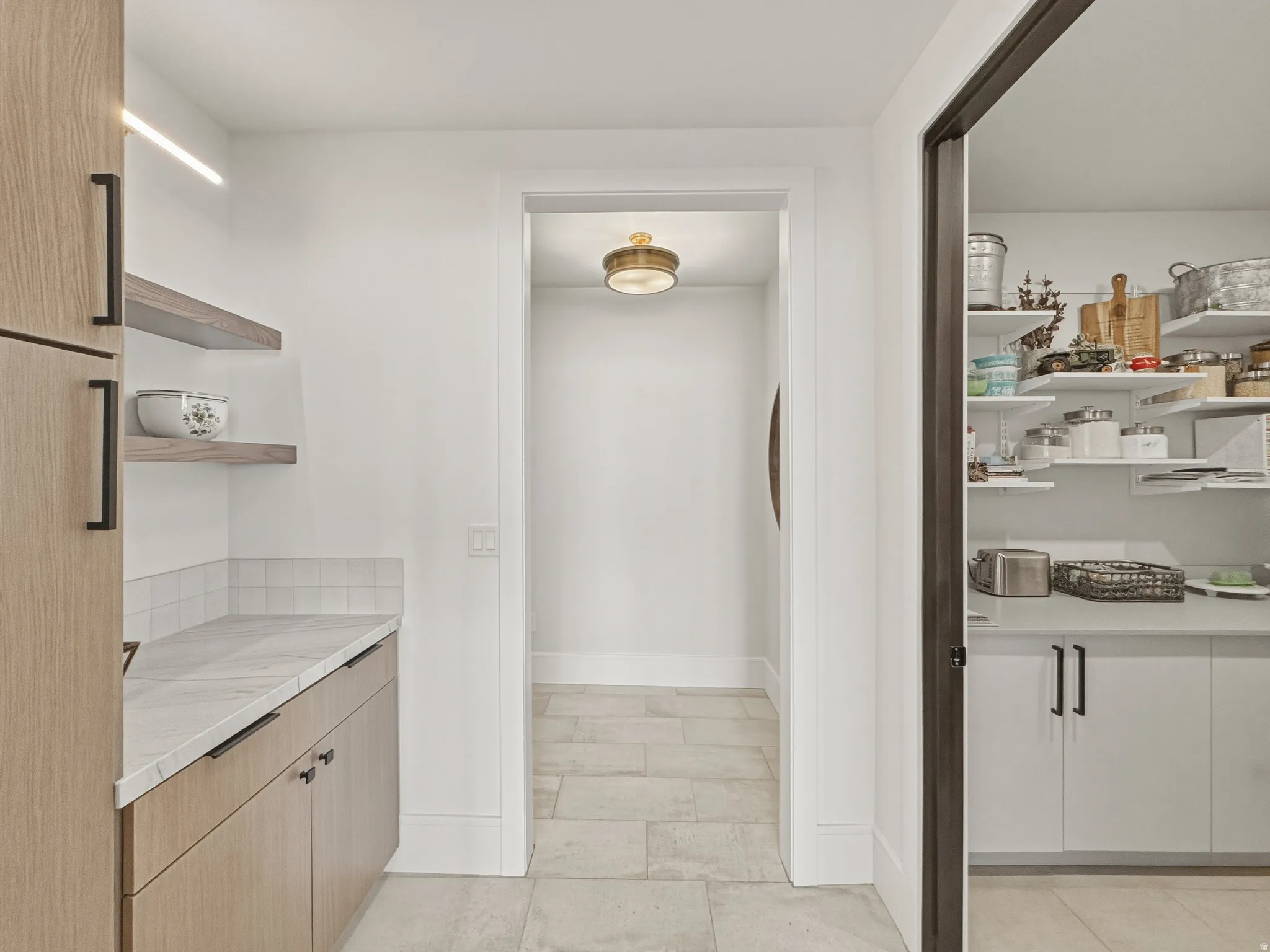 Kitchen pantry with light wood-finish cabinetry, white countertop, and white subway tile backsplash