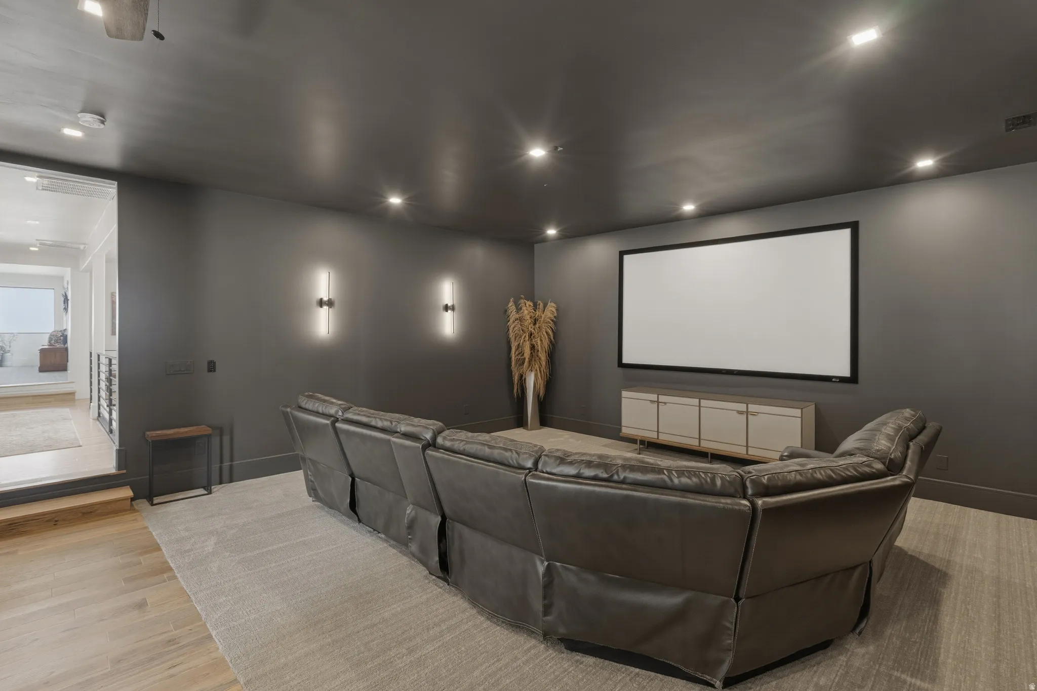 Dedicated media room featuring a large projection screen, recessed ceiling lighting, and two wall-mounted sconces
