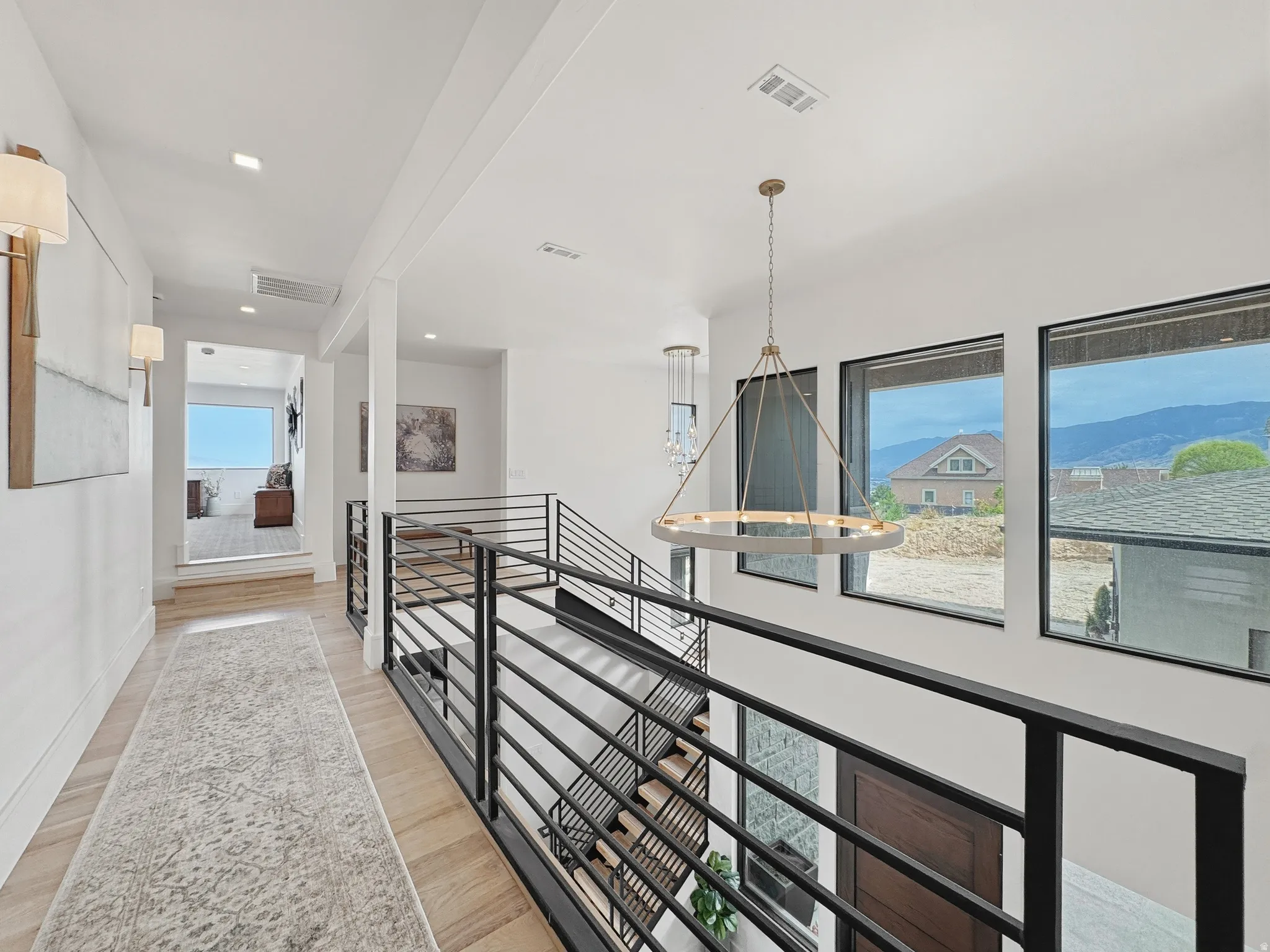 Upper-level hallway featuring light wood-finish flooring, recessed lighting, and modern wall sconces