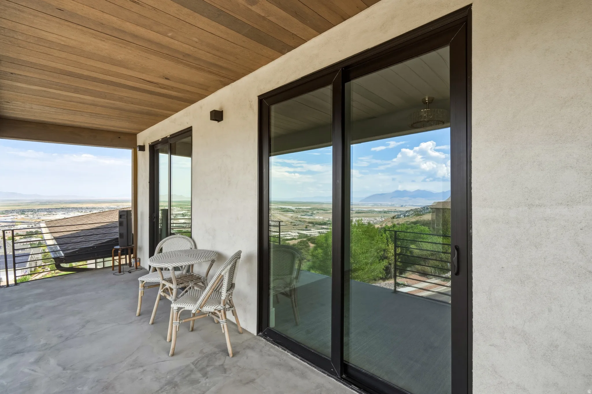 Expansive balcony featuring a concrete surface, wood-paneled ceiling, and glass sliding doors with dark frames