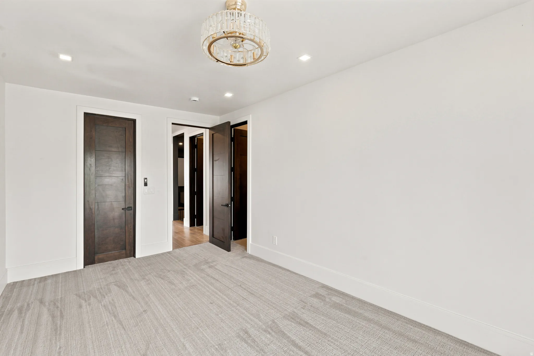 Bright room featuring a crystal chandelier, recessed lighting, light-toned carpeting, and dark wood-finish interior doors