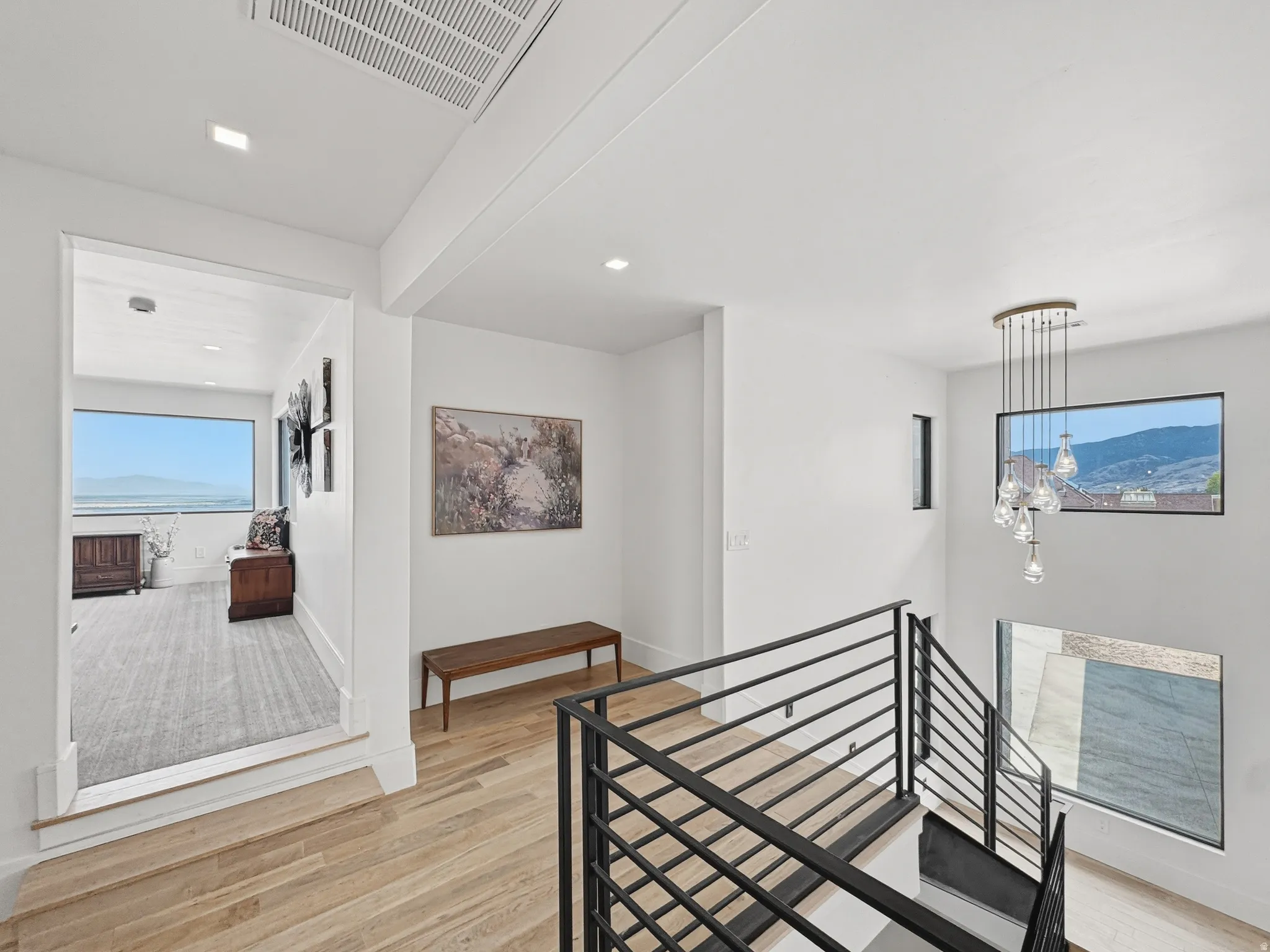 Hardwood flooring extending through a brightly lit hallway, featuring recessed lighting and a contemporary chandelier