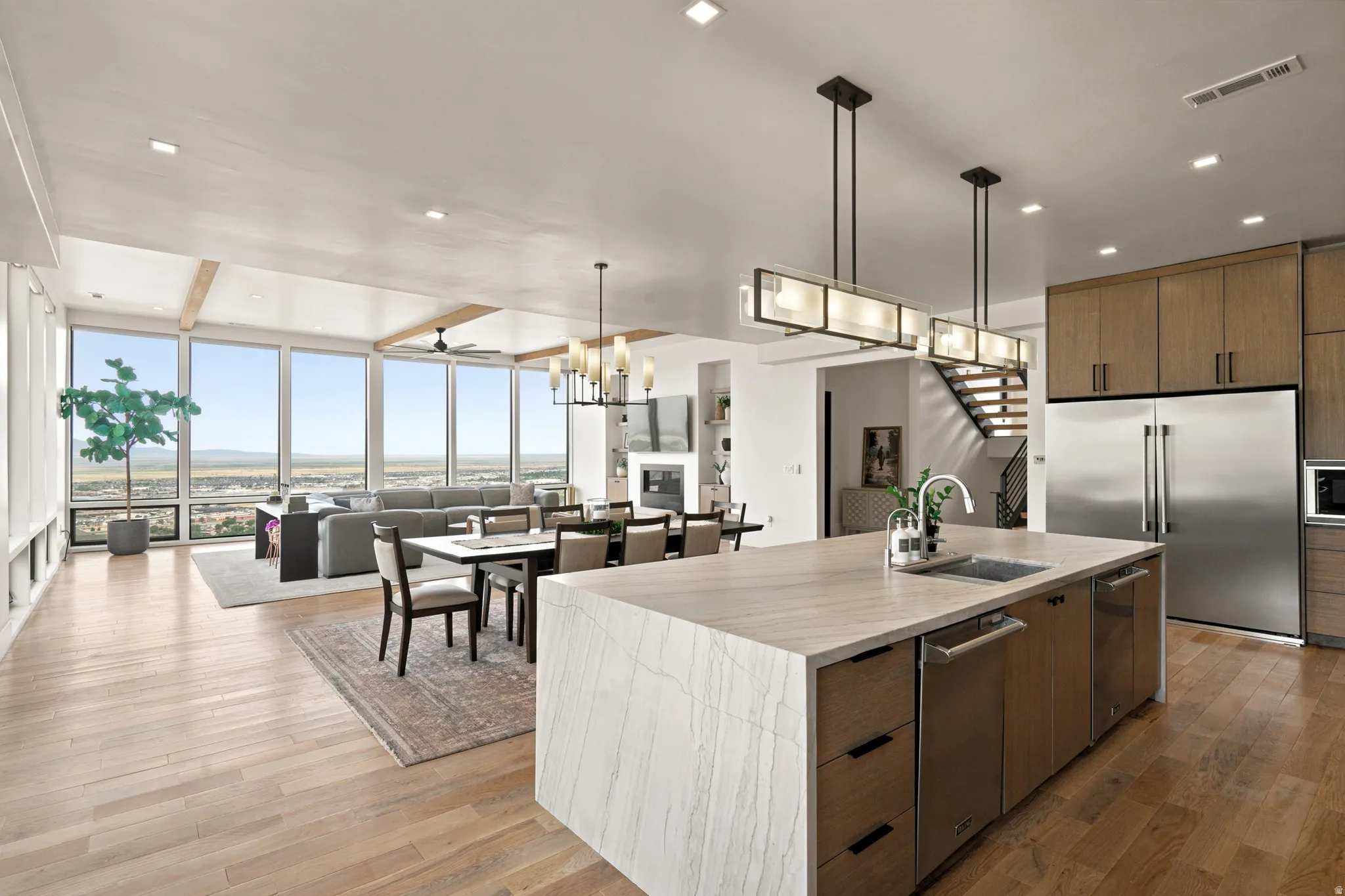 Open-concept living space featuring wood-finish flooring, a kitchen island with integrated sink, stainless steel appliances, and a wall of windows