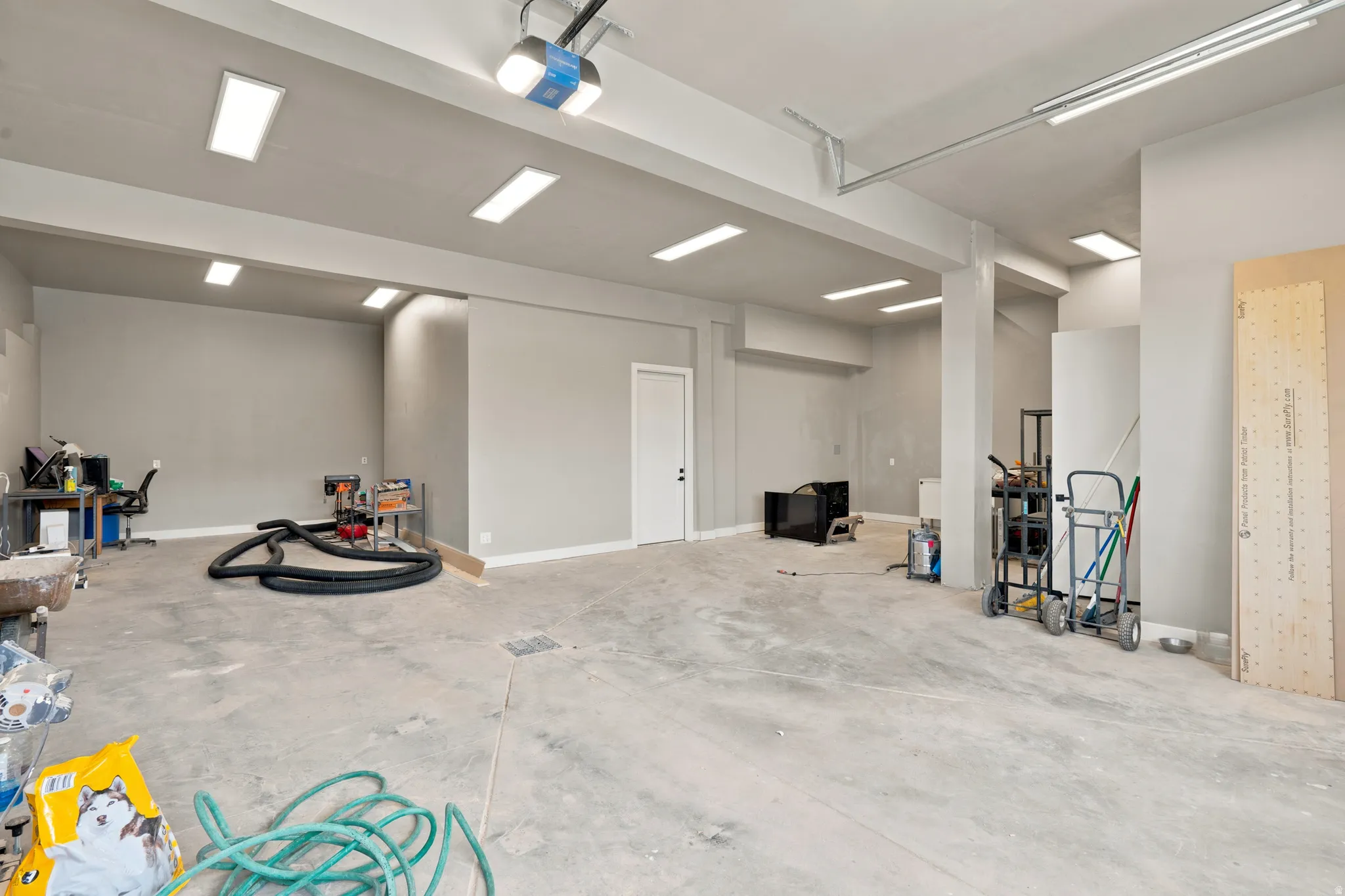 Spacious garage featuring a concrete floor, abundant overhead fluorescent lighting, and a garage door opener