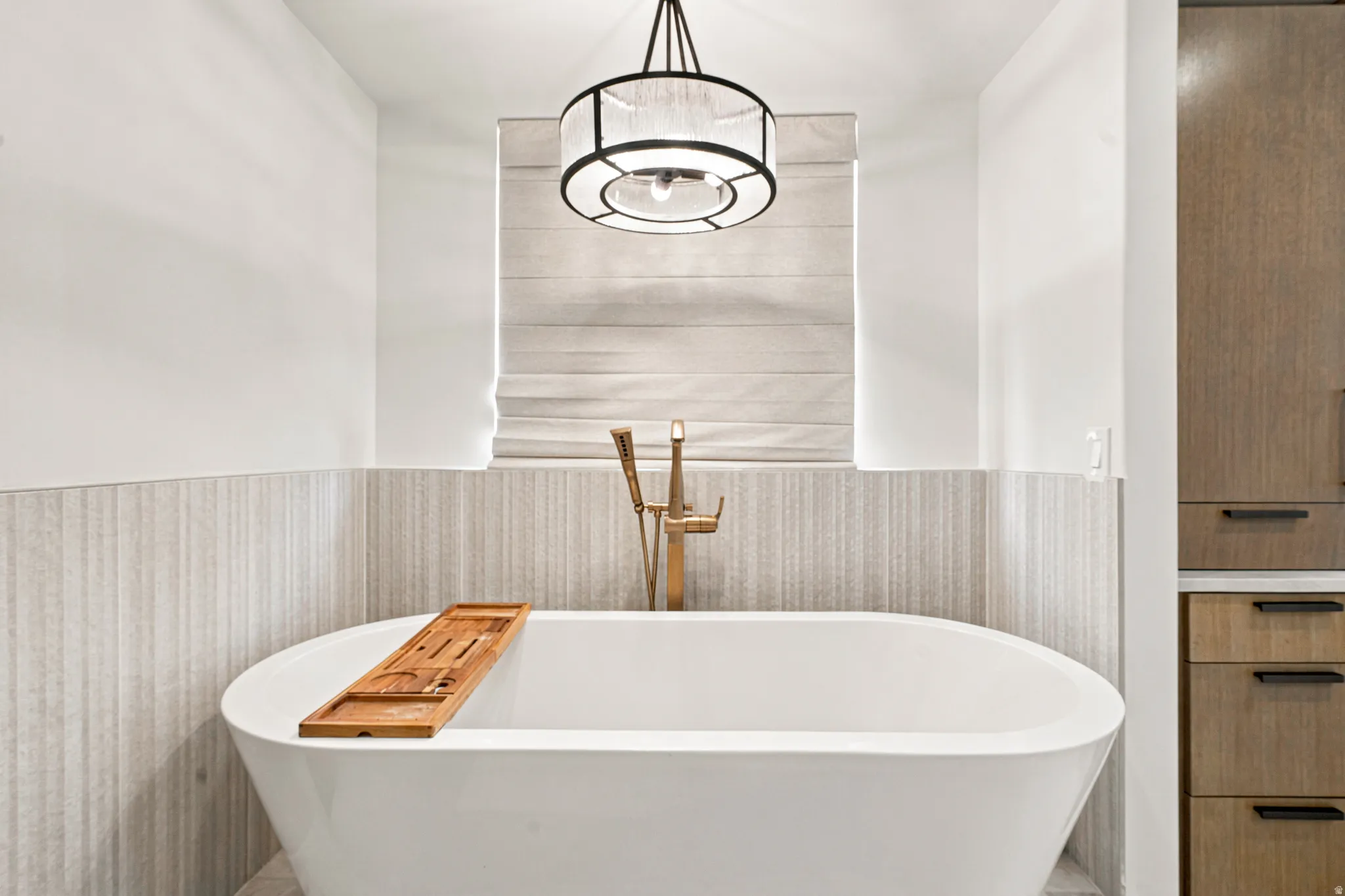 Freestanding soaking tub with floor-mounted brass faucet, textured accent wall, and a drum pendant light fixture