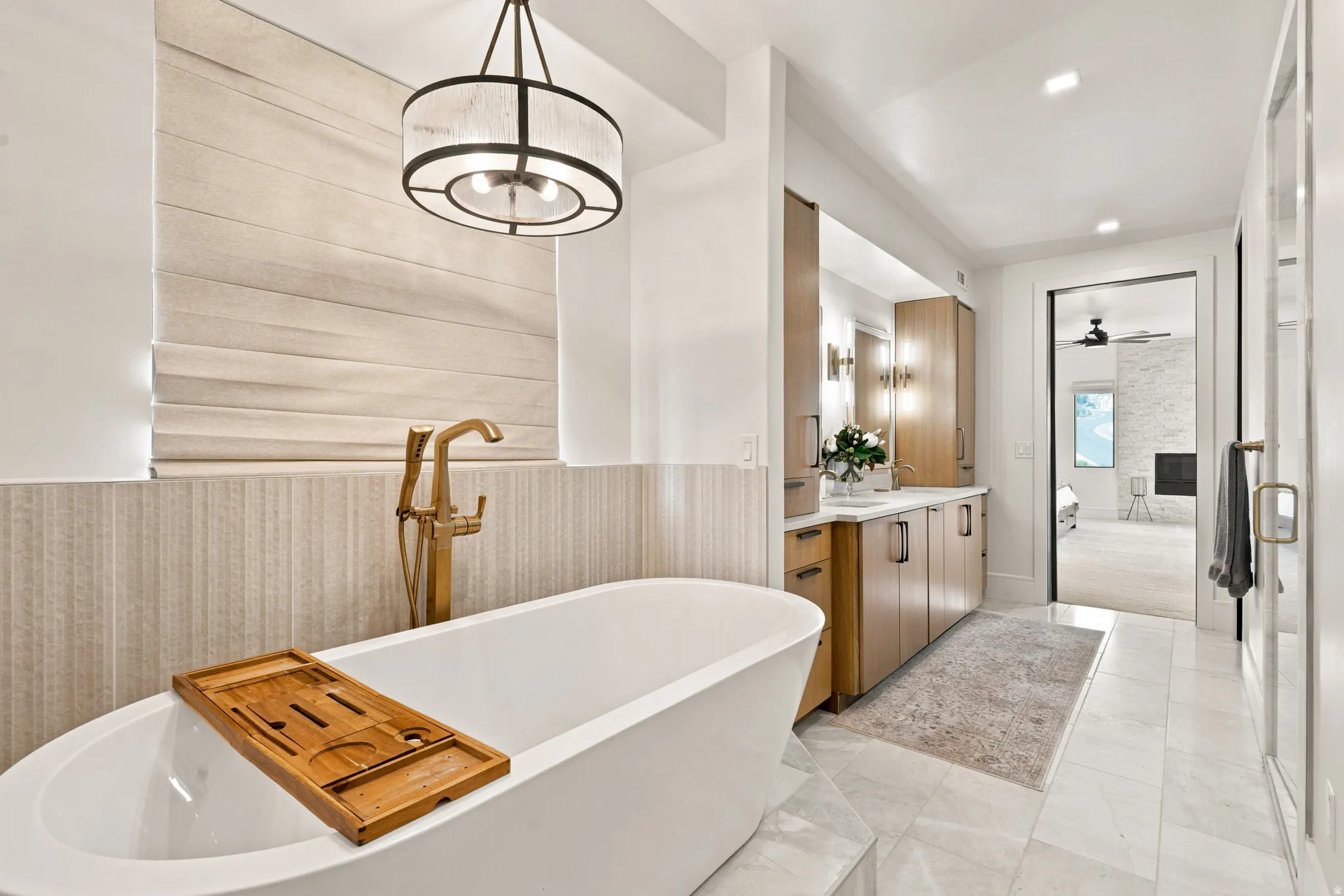 Freestanding soaking tub with brushed gold fixture, complemented by a dual vanity with light wood cabinetry and white countertops