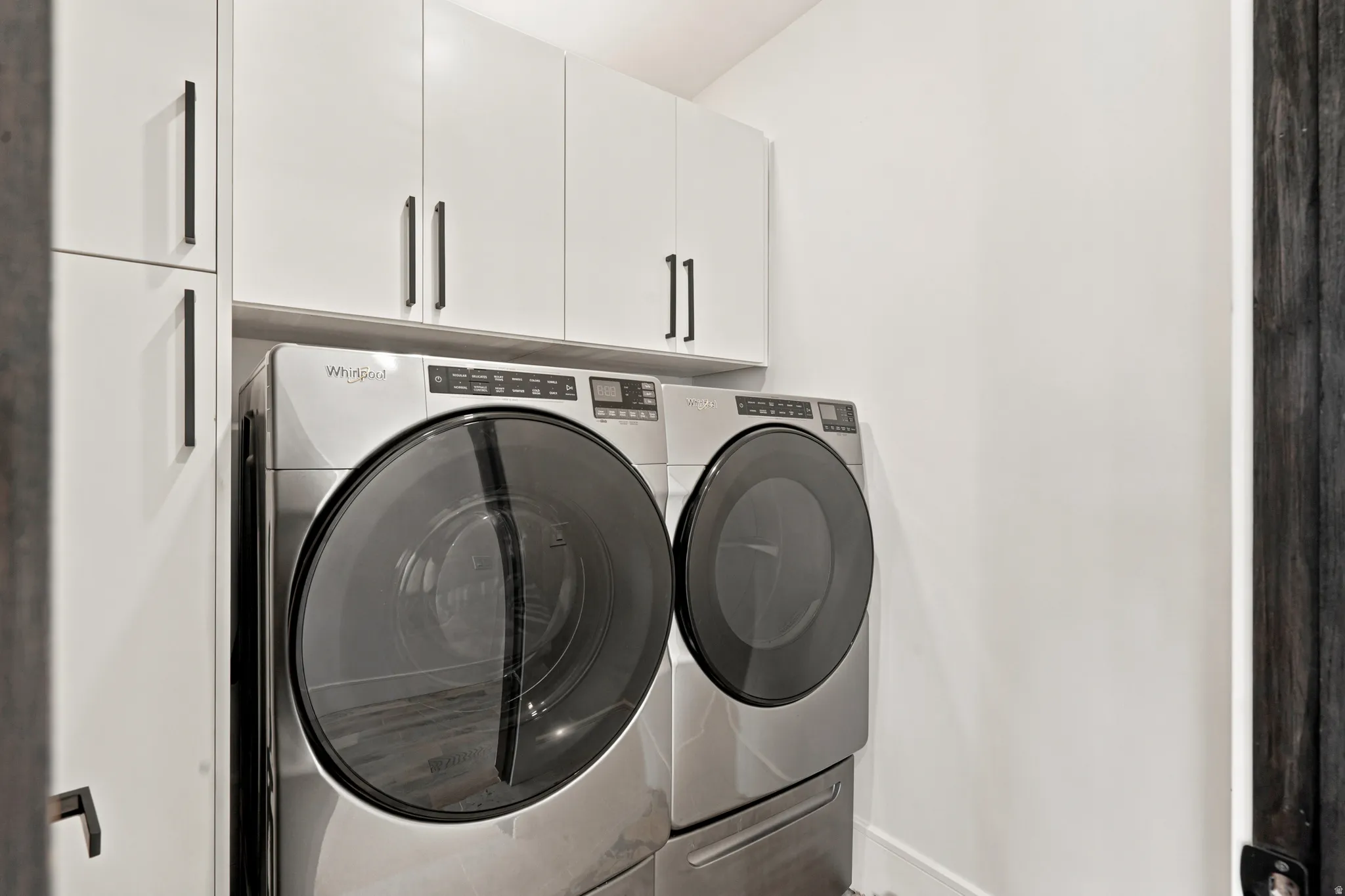 Dedicated laundry space featuring a side-by-side washer and dryer, white upper cabinetry, and dark hardware
