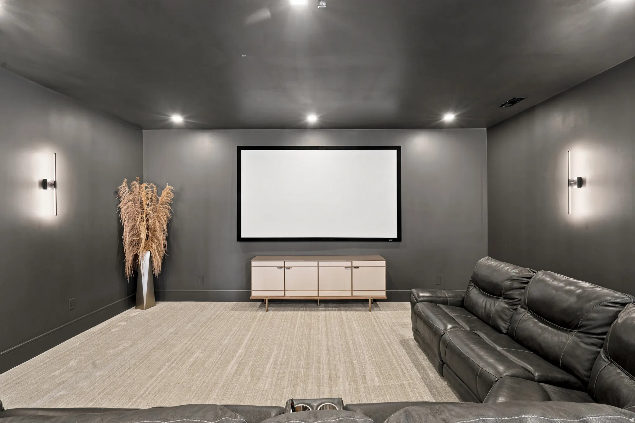 Dedicated media room featuring a large projection screen, recessed ceiling lighting, and modern wall sconces