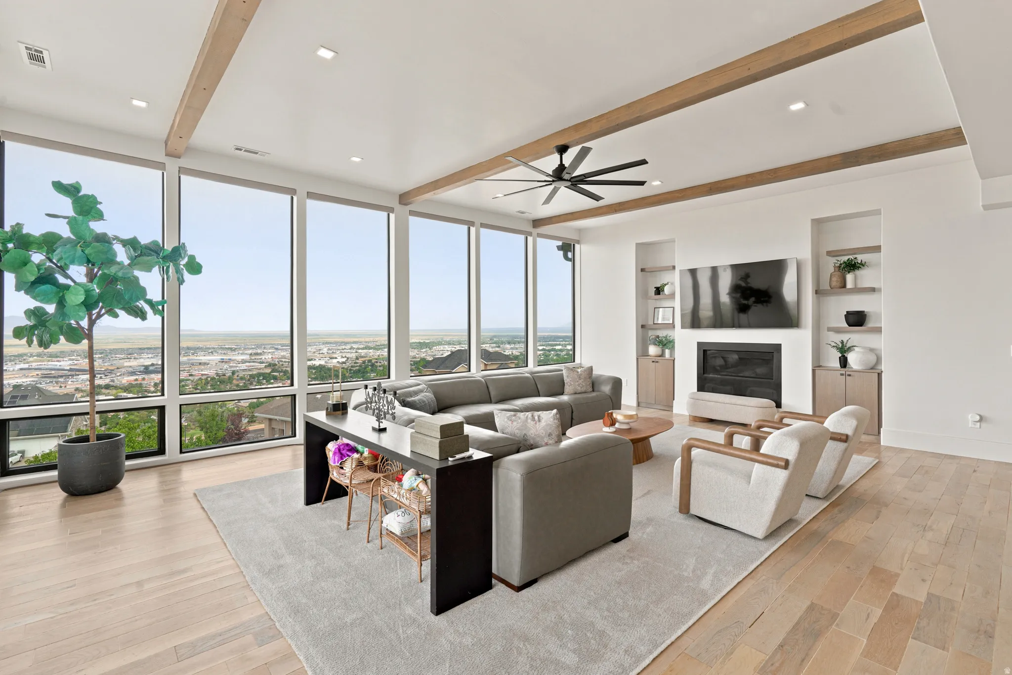 Spacious living area featuring expansive floor-to-ceiling windows, wood-finish flooring, and exposed ceiling beams