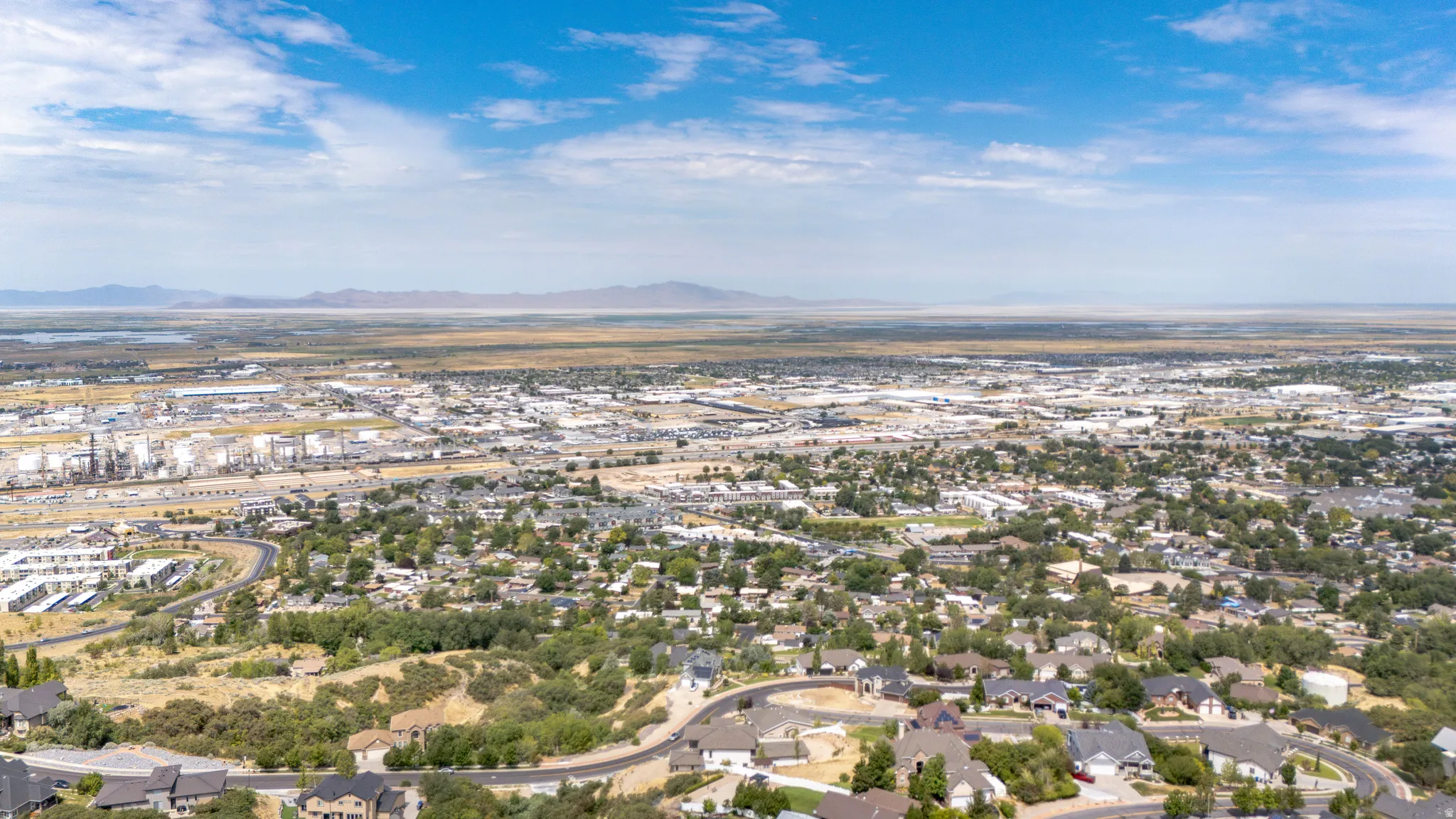 Expansive aerial perspective showcasing a developed landscape with residential areas, commercial zones, and distant mountain ranges under a clear sky