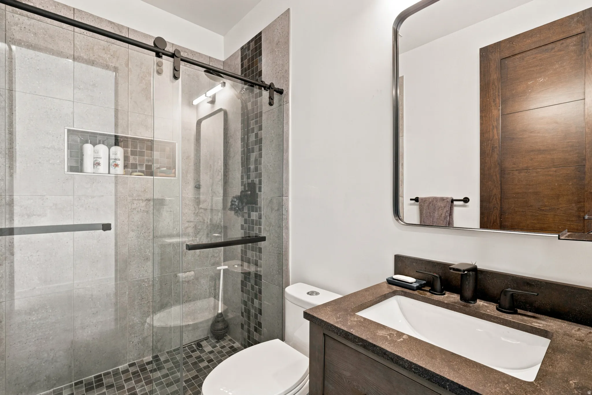 Modern bathroom featuring a glass-enclosed shower with a barn door style track, large format gray wall tiling, and a mosaic tile shower floor