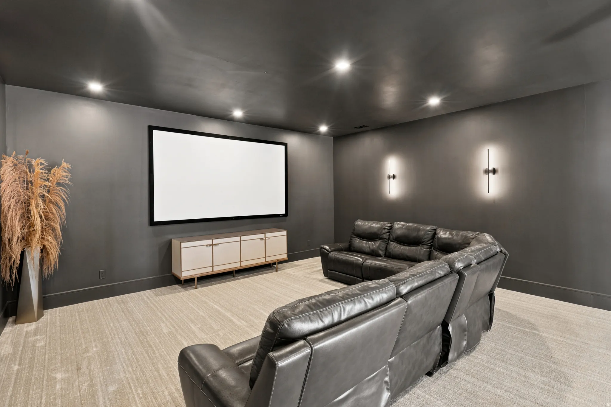 Dedicated media room featuring a large projection screen, recessed lighting, and wall-mounted sconces