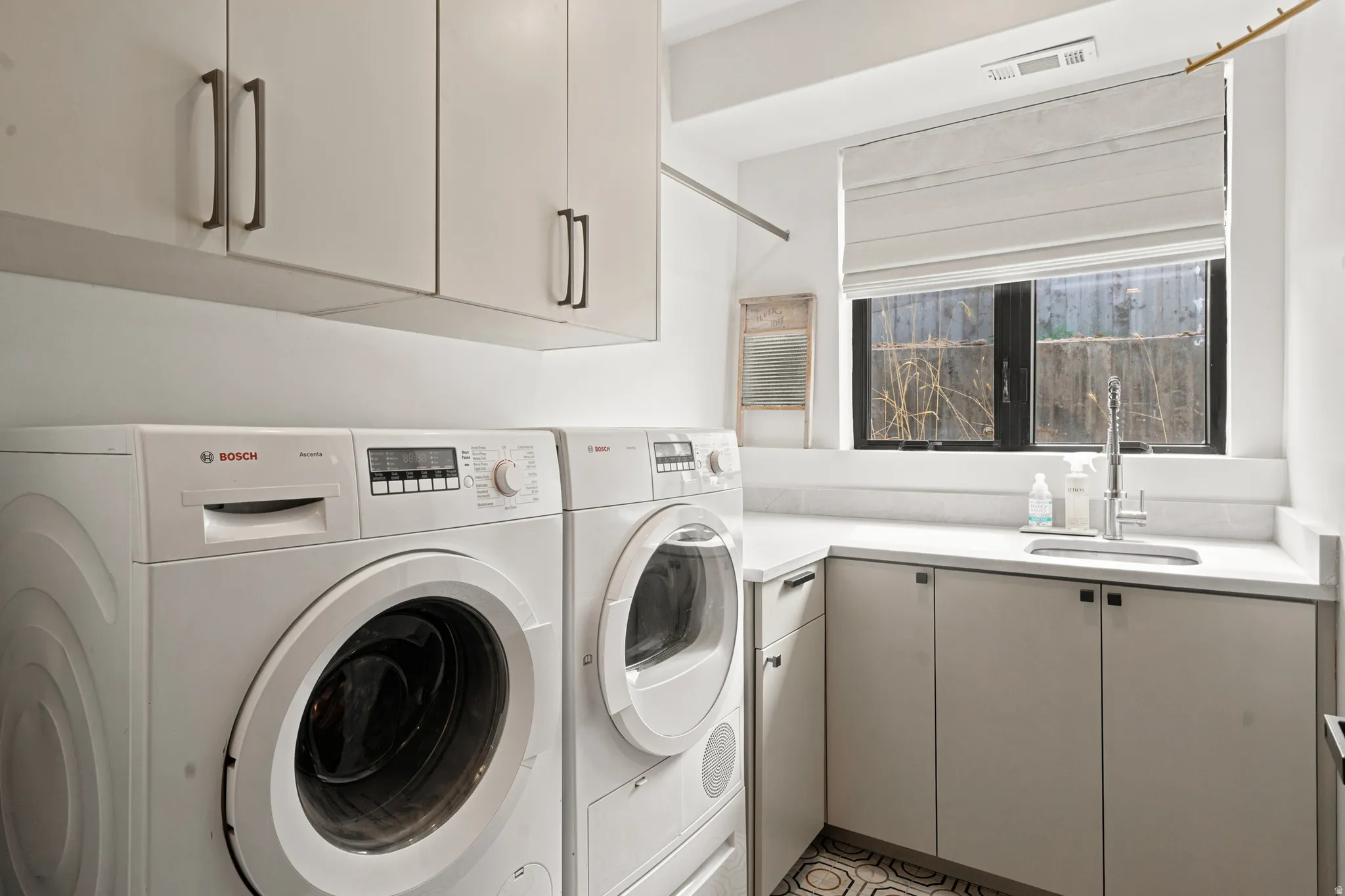 Dedicated laundry area featuring a built-in countertop, undermount sink with gooseneck faucet, upper and lower cabinetry, and tiled flooring