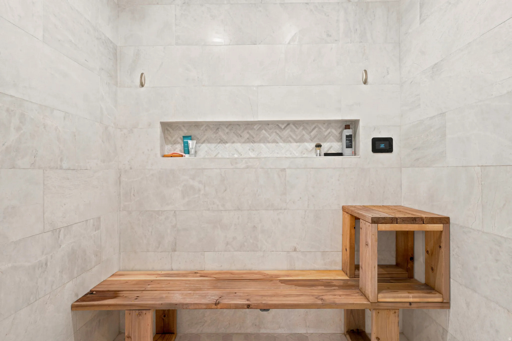 Shower enclosure featuring light-toned large format tile walls, a built-in wooden bench, and a recessed niche with a chevron-patterned tile accent