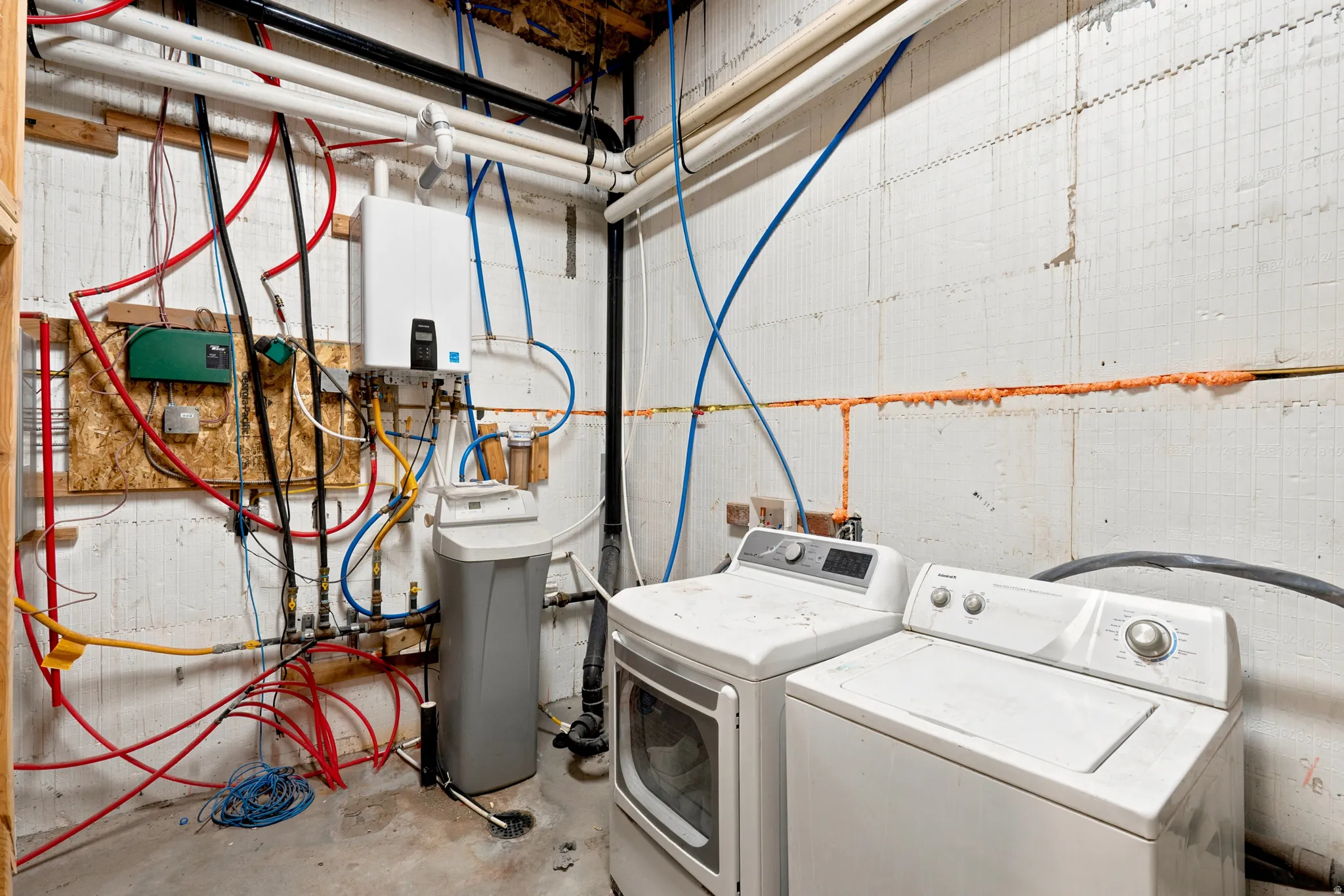 Utility area featuring a tankless water heater, water softener system, and exposed PEX plumbing