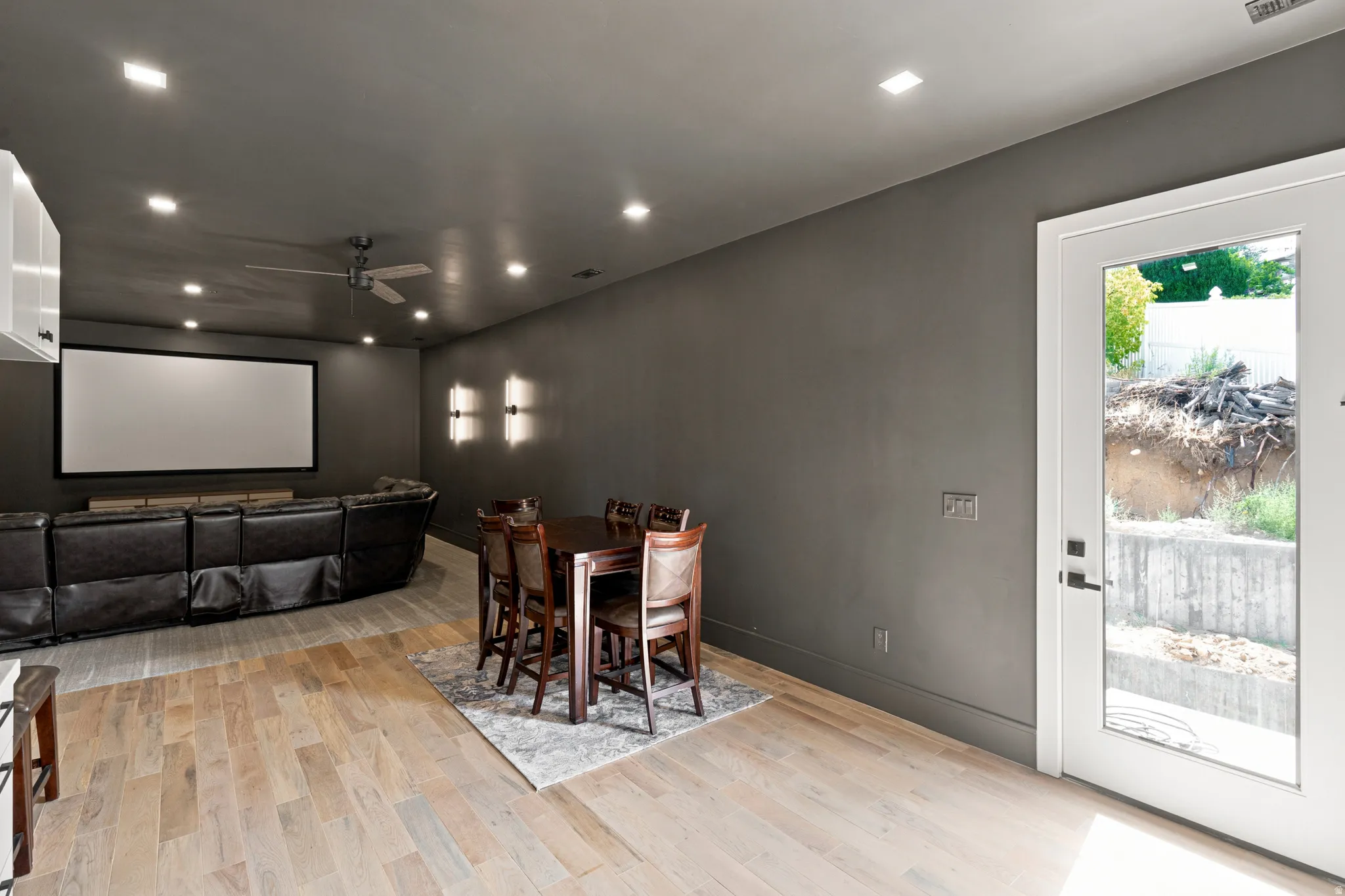 Spacious entertainment room featuring light wood-finish flooring, recessed lighting, and a prominent projection screen
