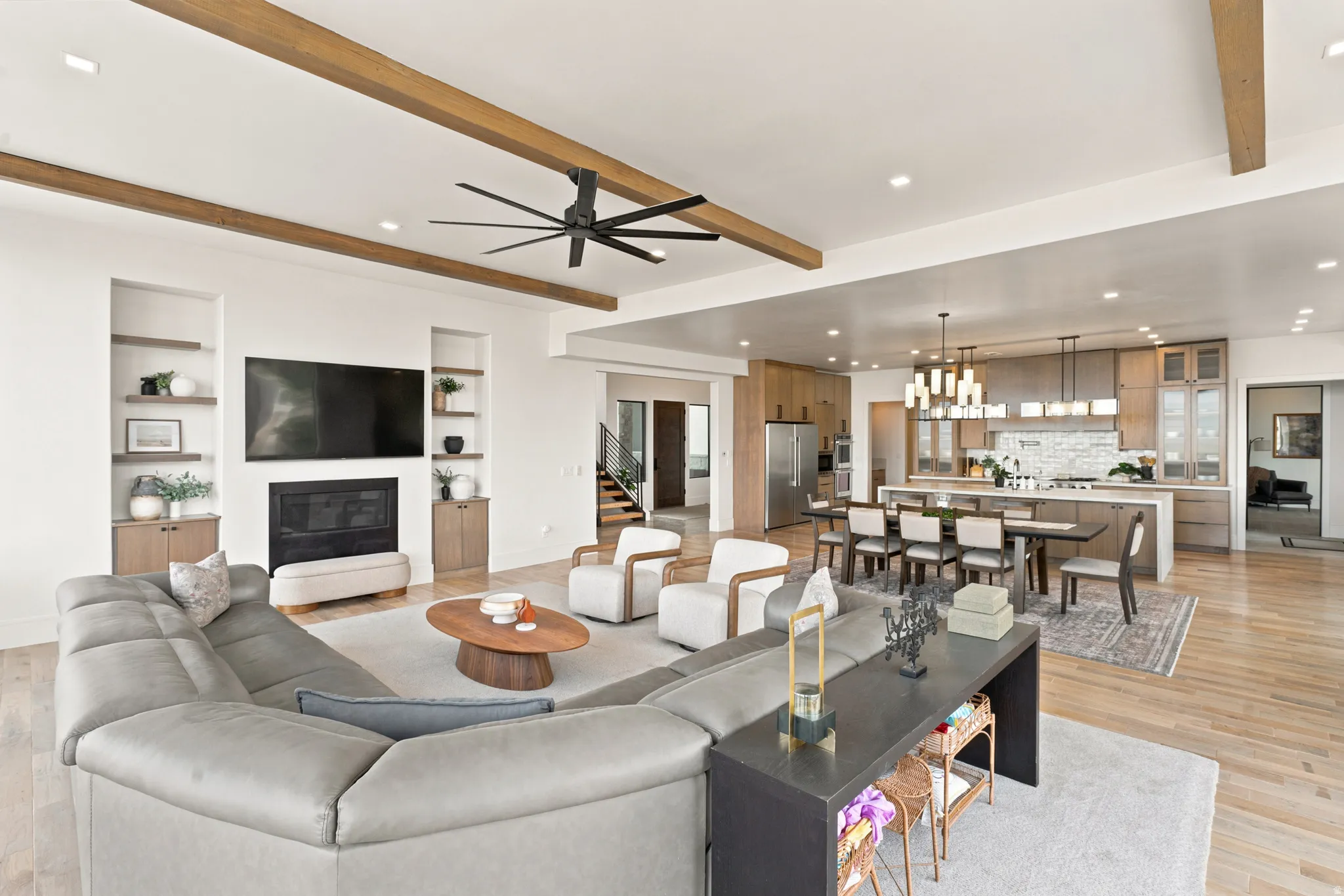 Open-concept living space featuring wood-finish flooring, exposed ceiling beams, and recessed lighting