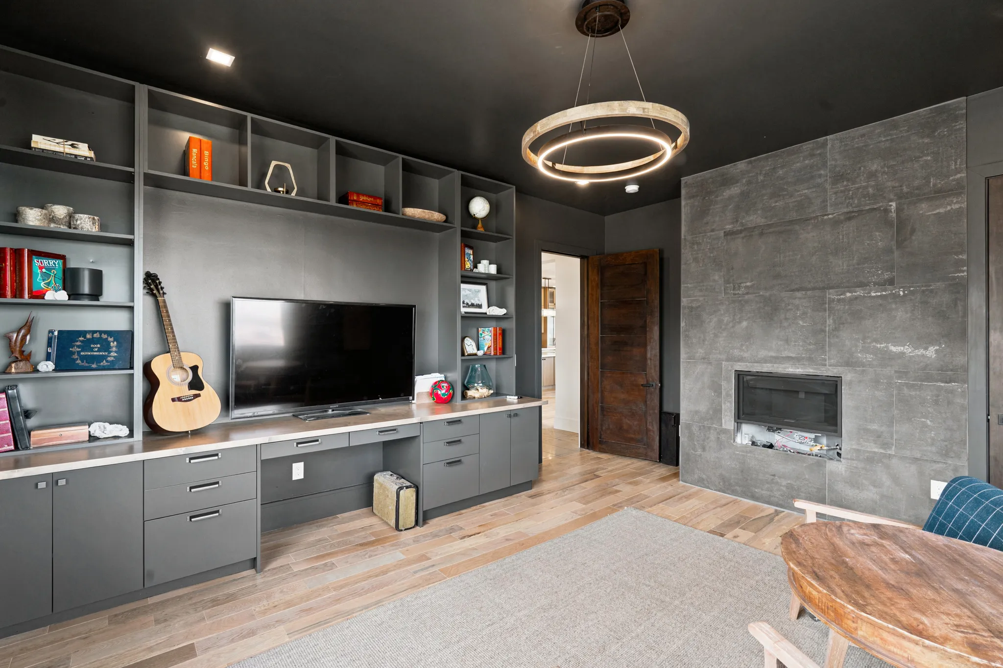 Built-in shelving and cabinetry with a light-colored countertop, stone fireplace surround, and wood-finish flooring