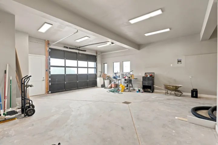 Spacious garage featuring a large glass-paneled overhead door, concrete flooring, multiple ceiling-mounted light fixtures, and a white side entry door
