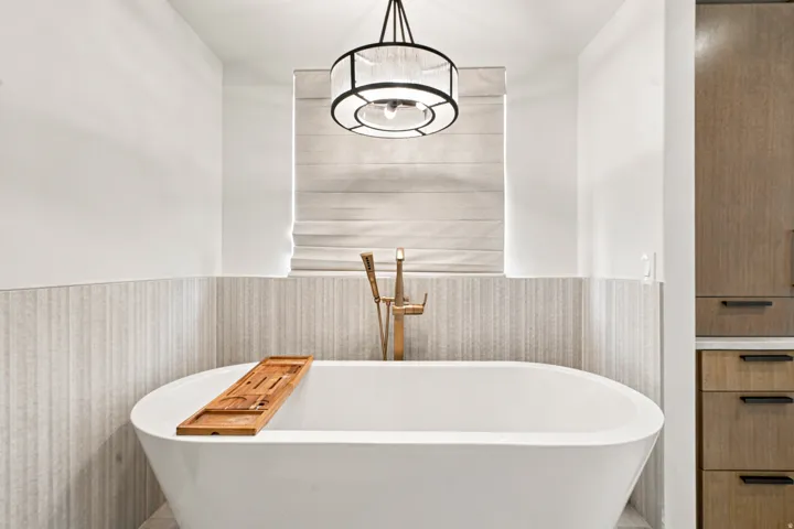 Freestanding soaking tub with floor-mounted brass faucet, textured accent wall, and a drum pendant light fixture