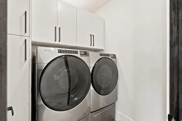 Dedicated laundry space featuring a side-by-side washer and dryer, white upper cabinetry, and dark hardware