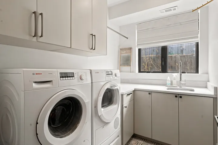 Dedicated laundry area featuring a built-in countertop, undermount sink with gooseneck faucet, upper and lower cabinetry, and tiled flooring